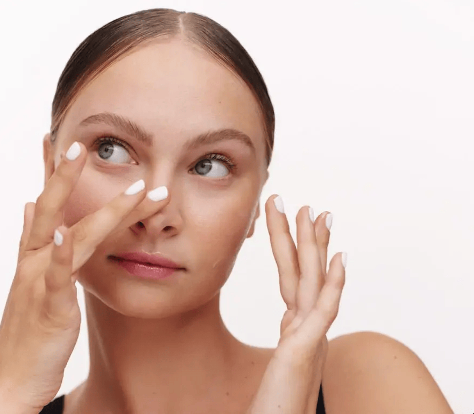 Person applying skincare product to their face with a neutral expression, against a white background. - K. Charles & Co. in San Antonio and Schertz, TX